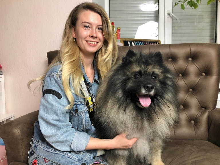 Дівчина в джинсовій куртці сидить на коричневому дивані з вульфшпіцом