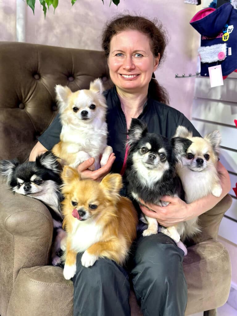 Жінка з підібраним волоссям сидить в грумерській формі в оточенні п'яти підстрижених чихів