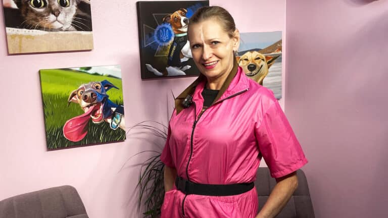 Жінка в рожевому комбінезоні для грумінгу позує біля смішних картин