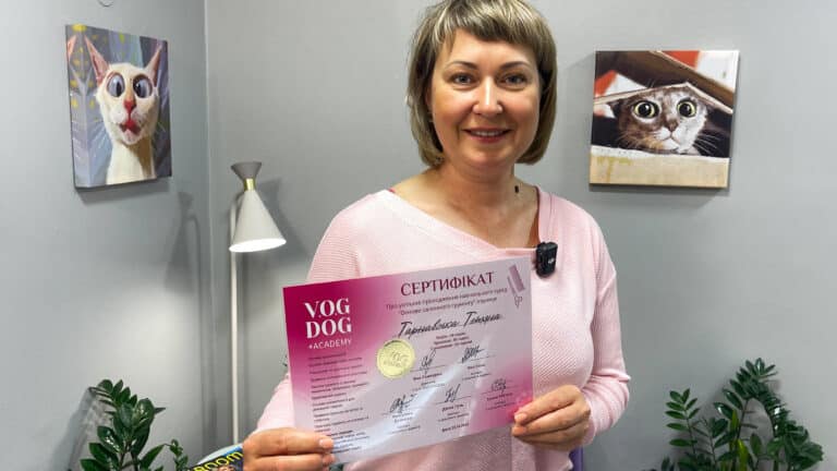 Жінка з короткою стрижкою тримає обома руками рожевий сертифіка