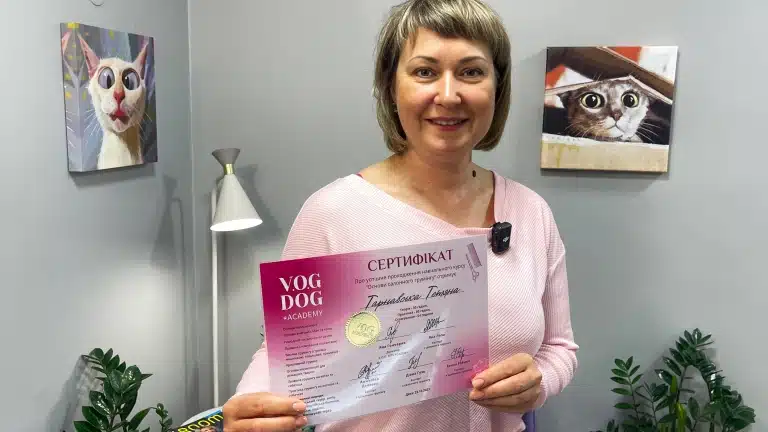 Жінка з короткою стрижкою тримає обома руками рожевий сертифіка