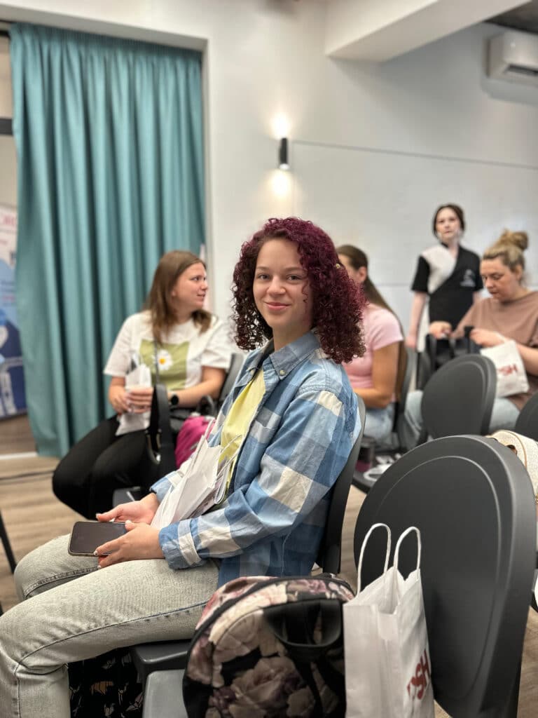 Дівчина з вишневими кучерями сидить на чорному стільці в очікуванні семінару