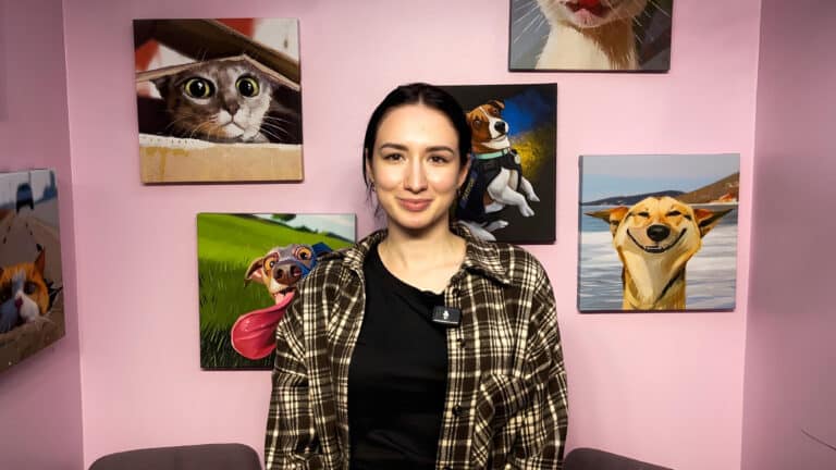 Перед картинами з собаками та котами стоїть дівчина в коричневій картатій сорочці