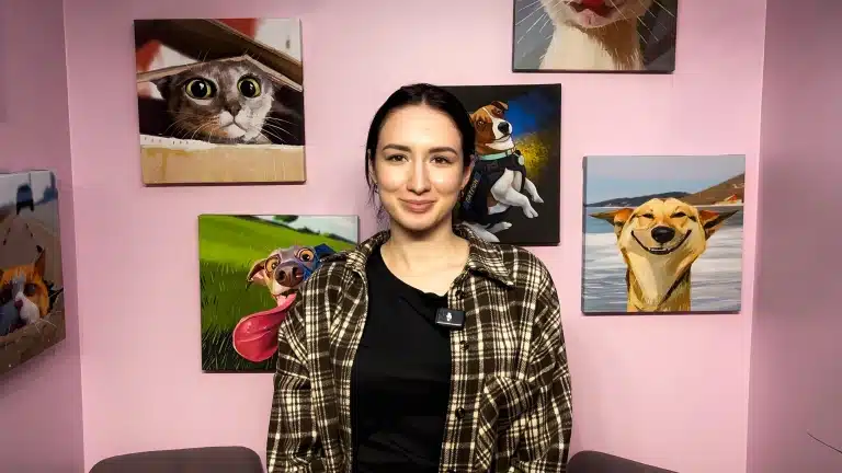 Перед картинами з собаками та котами стоїть дівчина в коричневій картатій сорочці