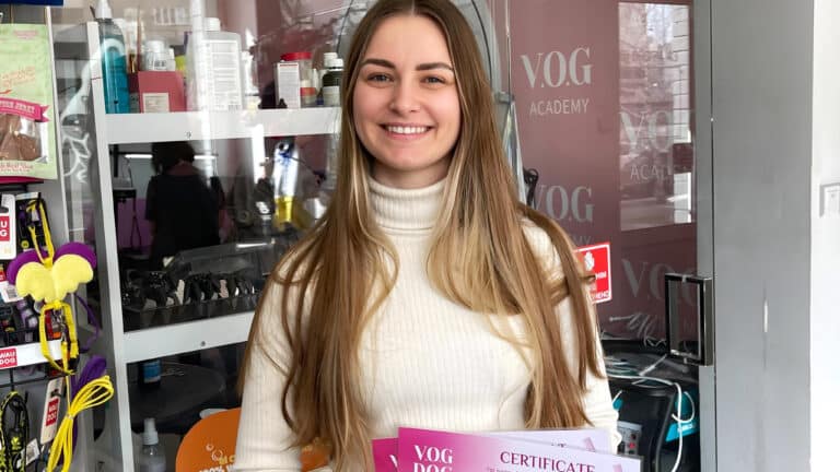 Дівчина з довгим волоссям вдягнута в світлу водолазку і стоїть біля грумерських інструментів