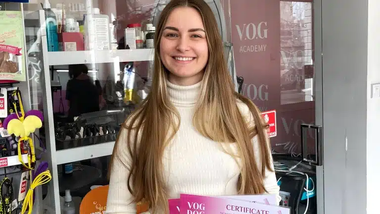 Дівчина з довгим волоссям вдягнута в світлу водолазку і стоїть біля грумерських інструментів