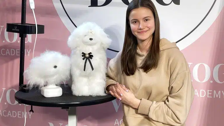 Дівчина з рівним волоссям обперлась на круглий стіл, на якому стоїть модель собаки з штучним хутром
