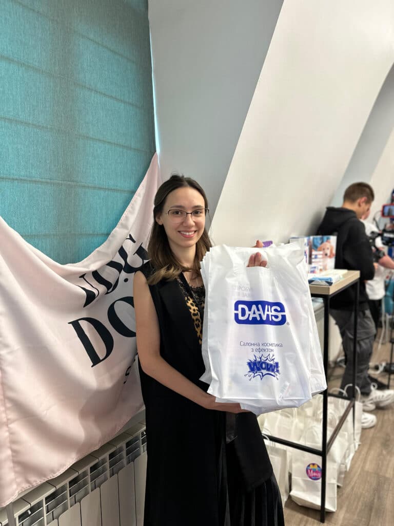 Дівчина в окулярах та леопардовій майці тримає в руках білі пакети з логотипом DAVIS