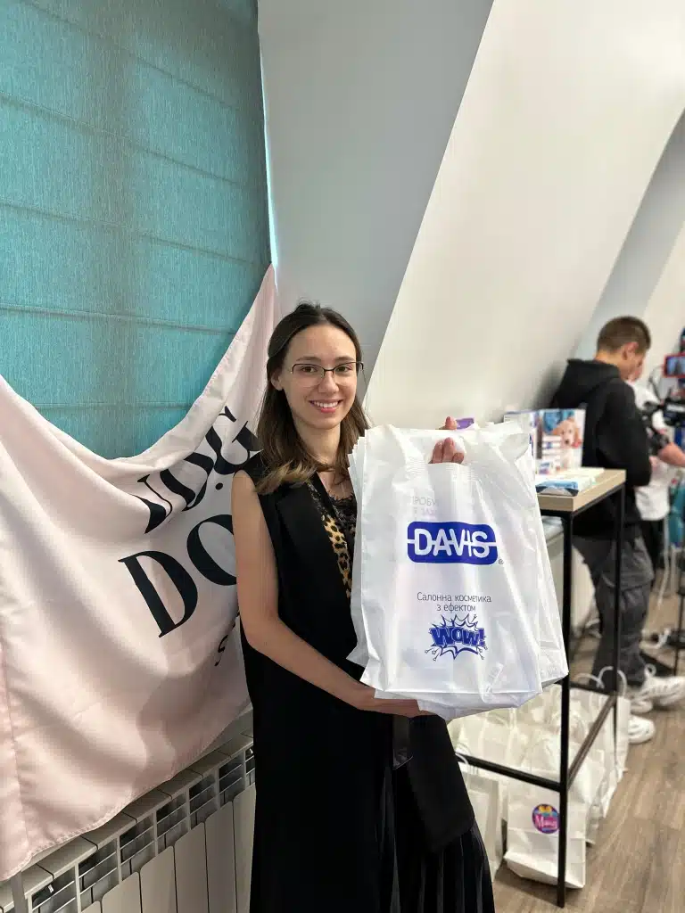 Дівчина в окулярах та леопардовій майці тримає в руках білі пакети з логотипом DAVIS