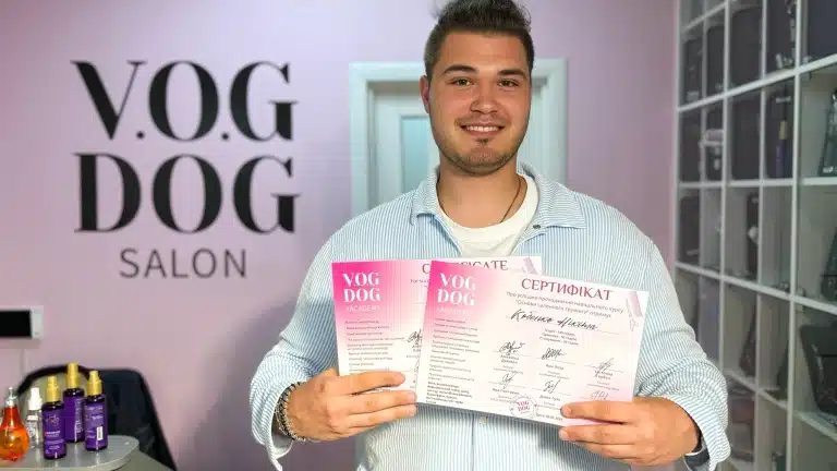 Хлопець в блакитній сорочці стоїть в салоні, тримаючи два сертифікати