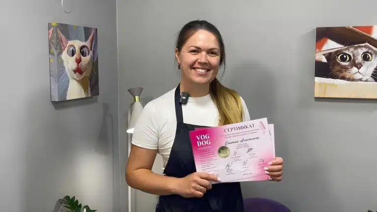 Праворуч і ліворуч від дівчини в чорному фартусі висять картини з світлими котами