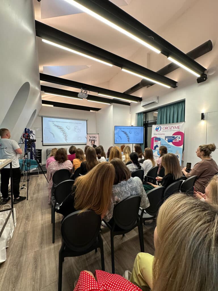 Дві дівчини схилилось одна до одної, прослуховуючи лекцію, запис якої ведеться на камеру