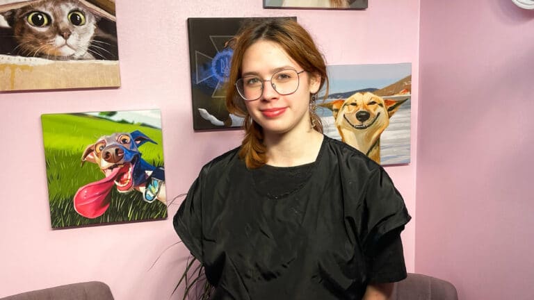 Дівчина в круглих окулярах стоїть біля картини собаки з довгим язиком