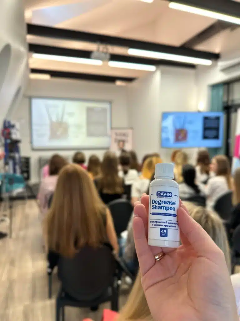 Маленька баночка шампуню сфотографована на фоні проведення грумерської лекції