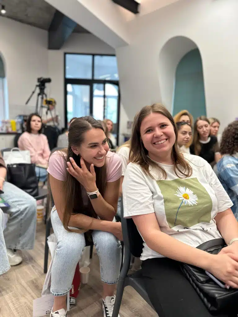 Дві дівчини, сидячи на стільцях, посміхаються під час своєї розмови в кімнаті