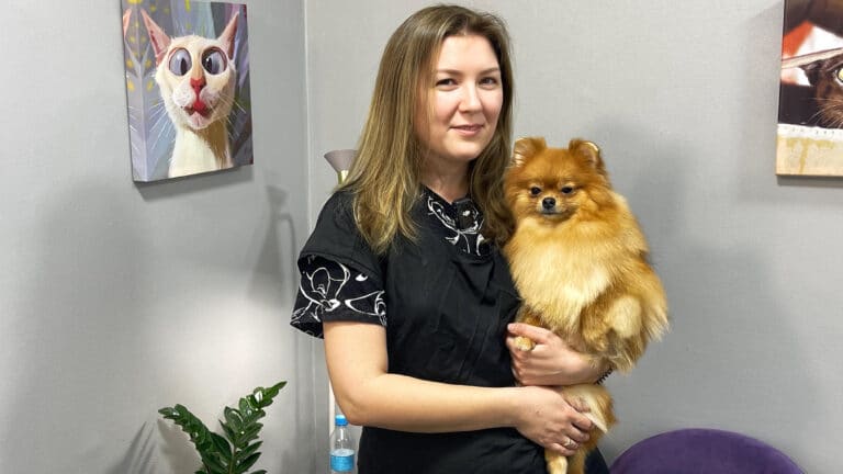 Рудий шпіц сидить на руках дівчини в чорній грумерській формі