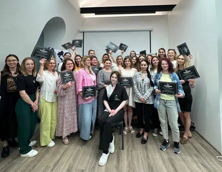 Позаду дівчини в чорно-білій формі зібрались вдячні учні з чорними сертифікатами в руках