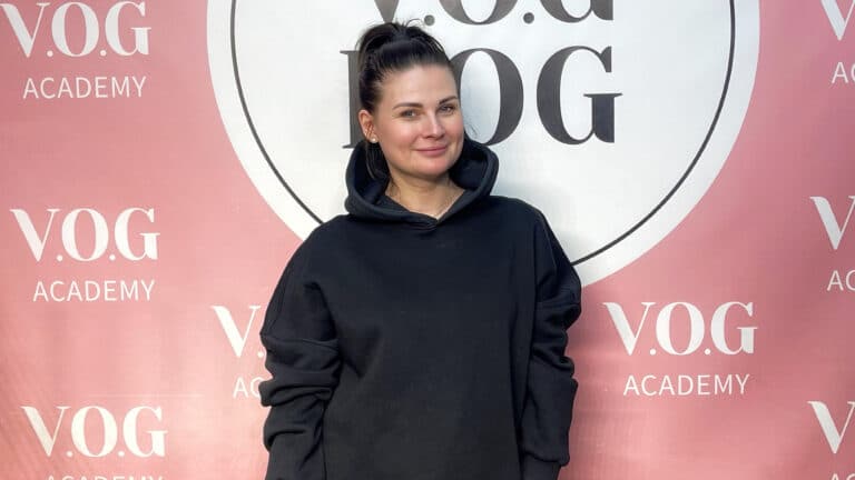 Дівчина в чорному светрі з капюшоном стоїть перед банером Академії