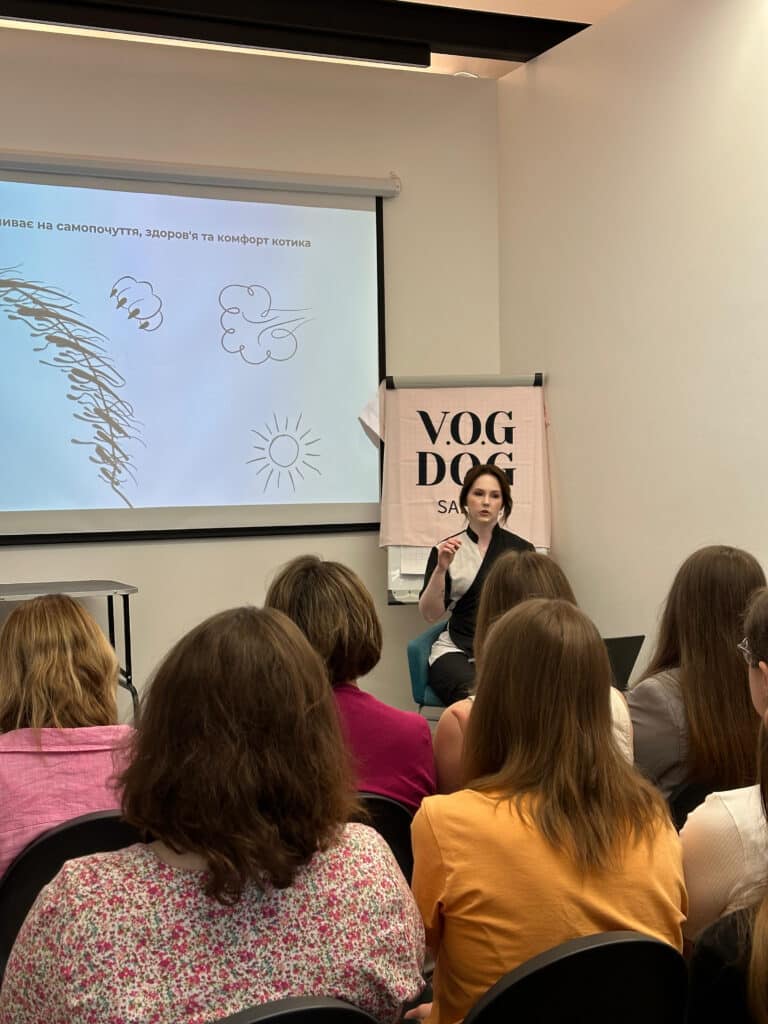 Перед аудиторію виступає дівчина в чорно-білій формі, жестикулюючи для кращої подачі матеріалу