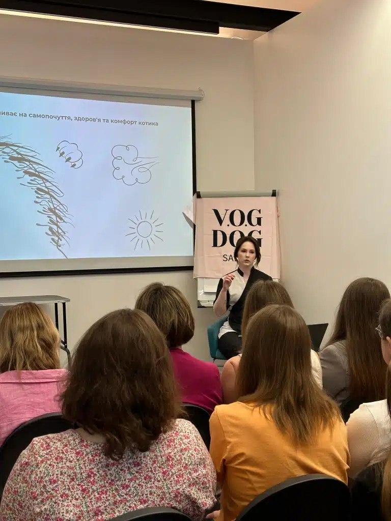 Перед аудиторію виступає дівчина в чорно-білій формі, жестикулюючи для кращої подачі матеріалу