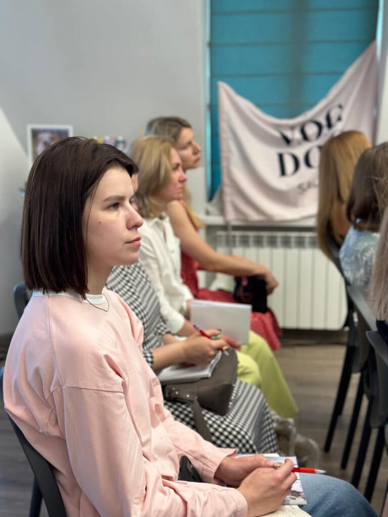 Дівчина з каре, вдягнута в рожеву кофтинку, зосереджено дивиться перед собою