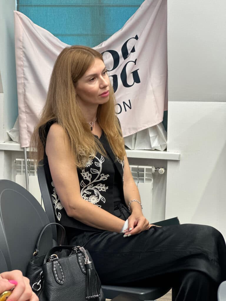 Дівчина в чорному костюмі з білим візерунком нахилила трохи голову, тримаючи руки на колінах