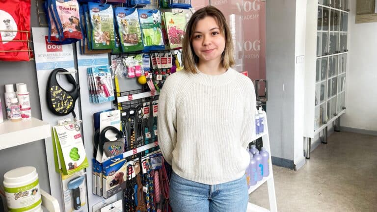 Дівчина в білому светрі стоїть біля стелажа зі смаколиками для собак