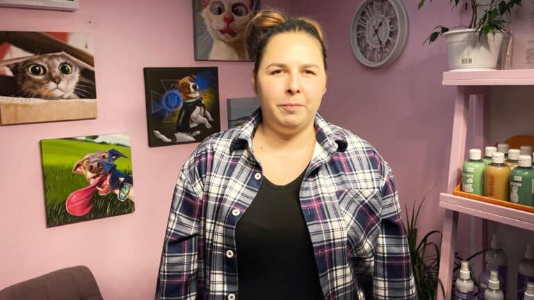 Дівчина в картатій сорочці та чорній майці стоїть біля стелажа з професійною косметикою