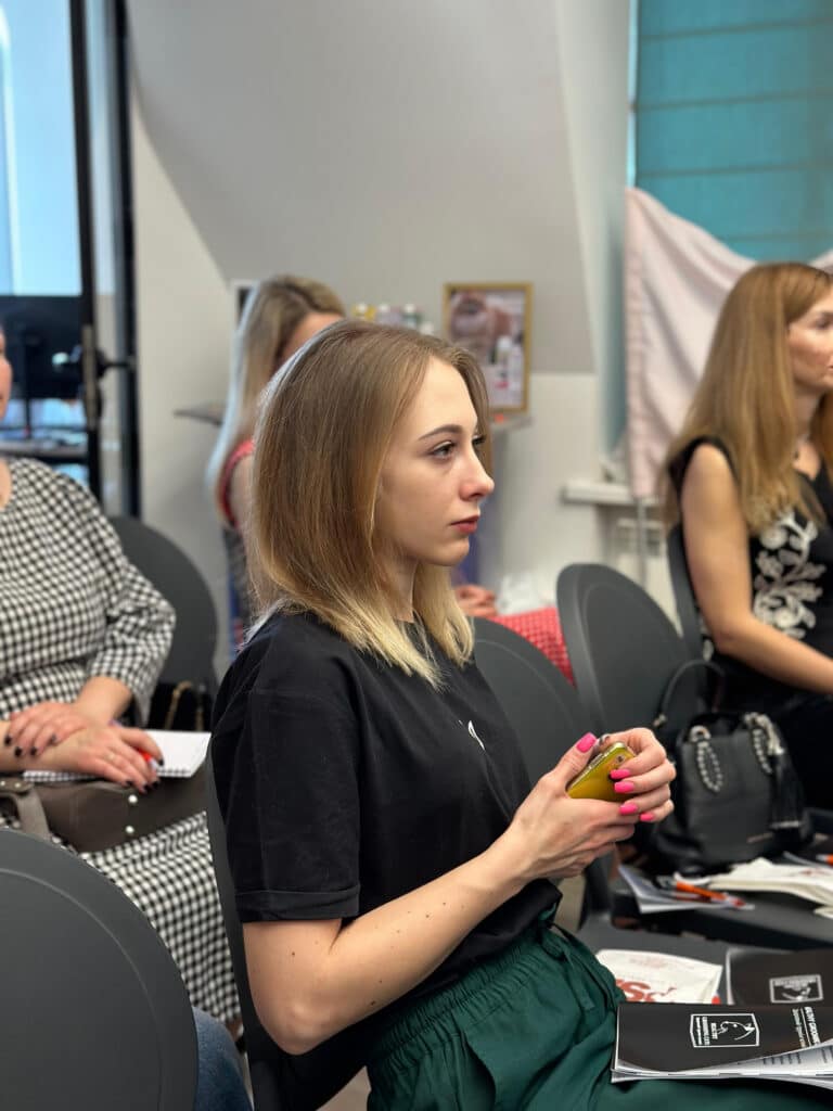 Дівчина в чорній футболці та темно-зелених штанах тримає в руках золотий телефон