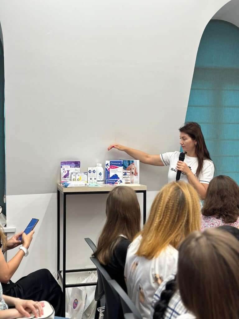 Жінка в білій футболці з використанням мікрофона розповідає про засоби Орозим для тварин