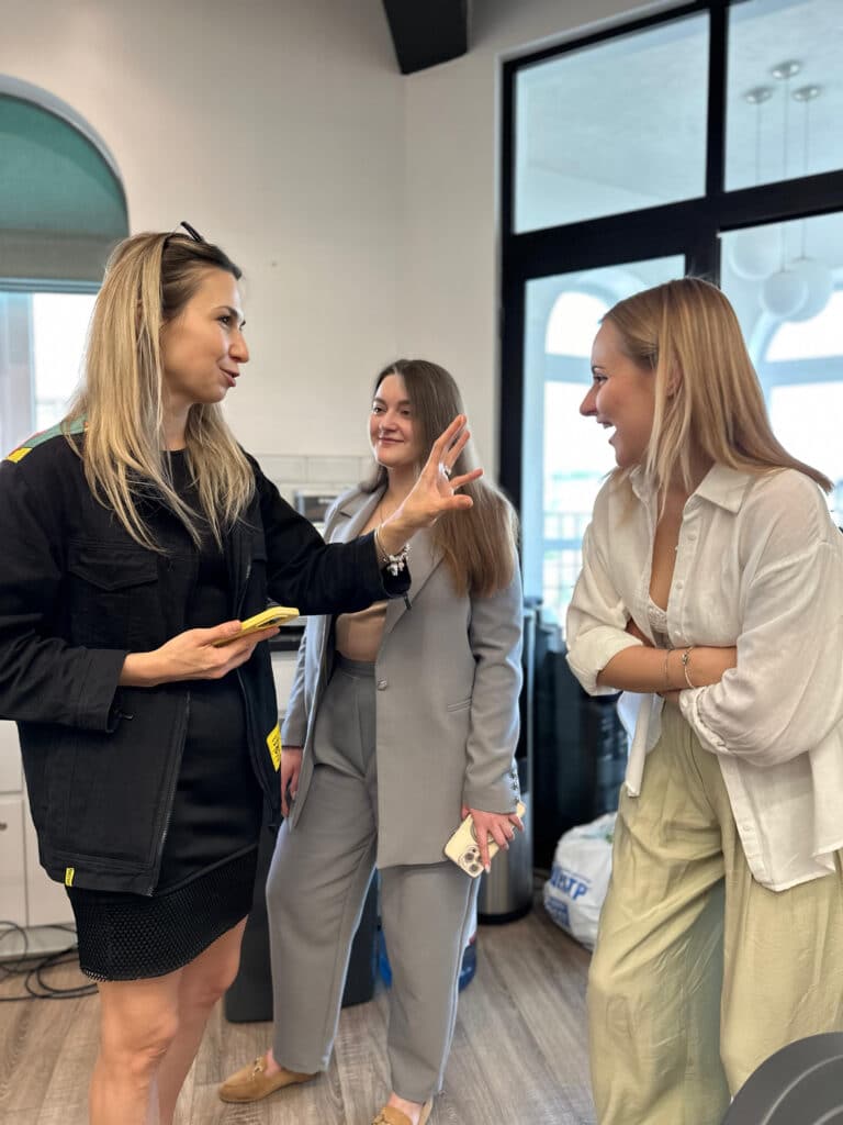 Дівчина в чорному розповідає щось смішне дівчині в лляному костюмі