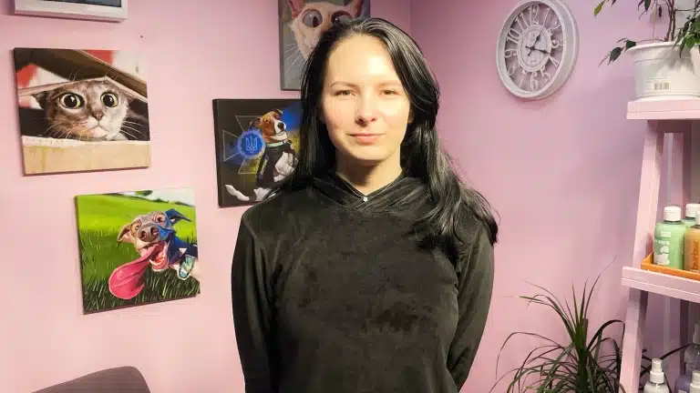 Дівчина в чорному одязі та з чорним волоссям сором'язливо стоїть перед камерою