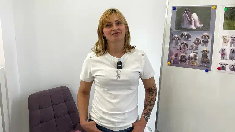 Дівчина в білій футболці стоїть біля сірого стільця в білій кімнаті