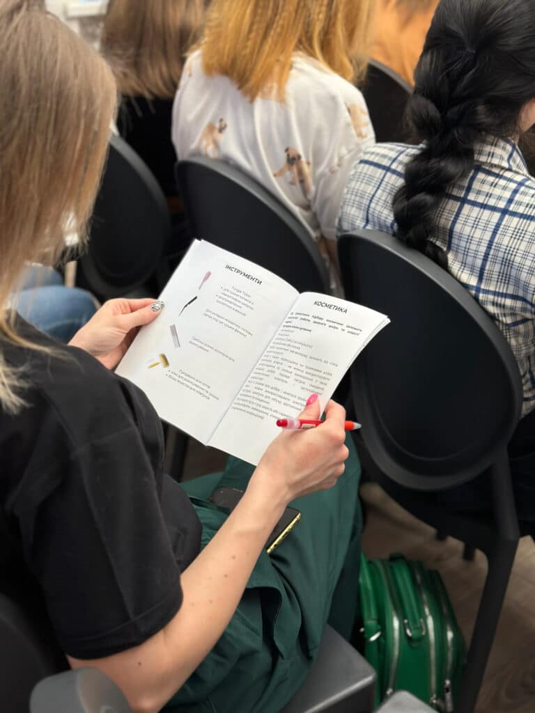 Дівчина в зелених штанах поклала біля ніг зелений рюкзак та читає брошуру