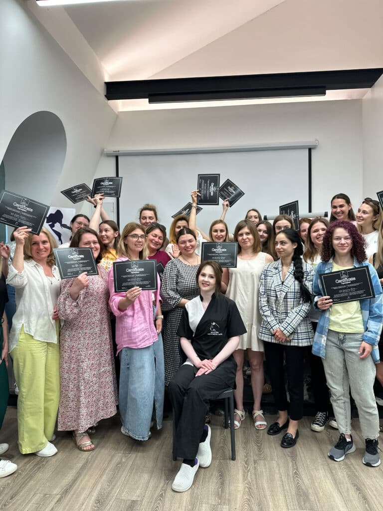 Щасливі грумери тримають чорні сертифікати, а перед ними на стільці посміхається викладачка