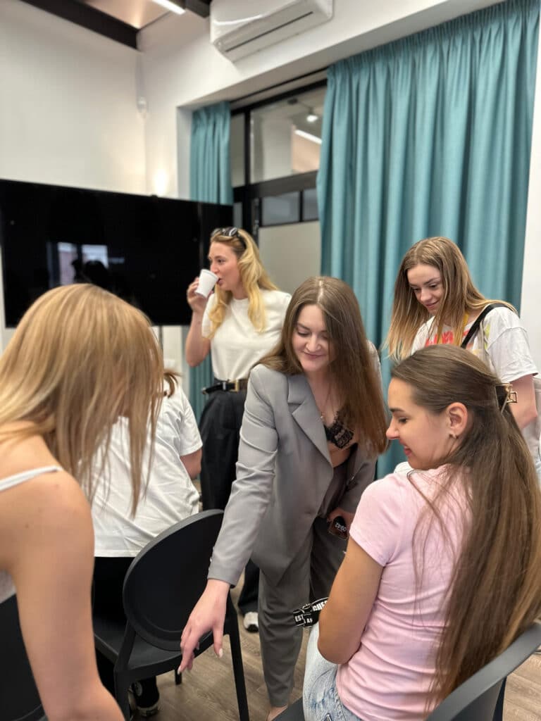 Дівчина в сірому костюмі на щось вказує, і інші дівчата дивляться в той бік