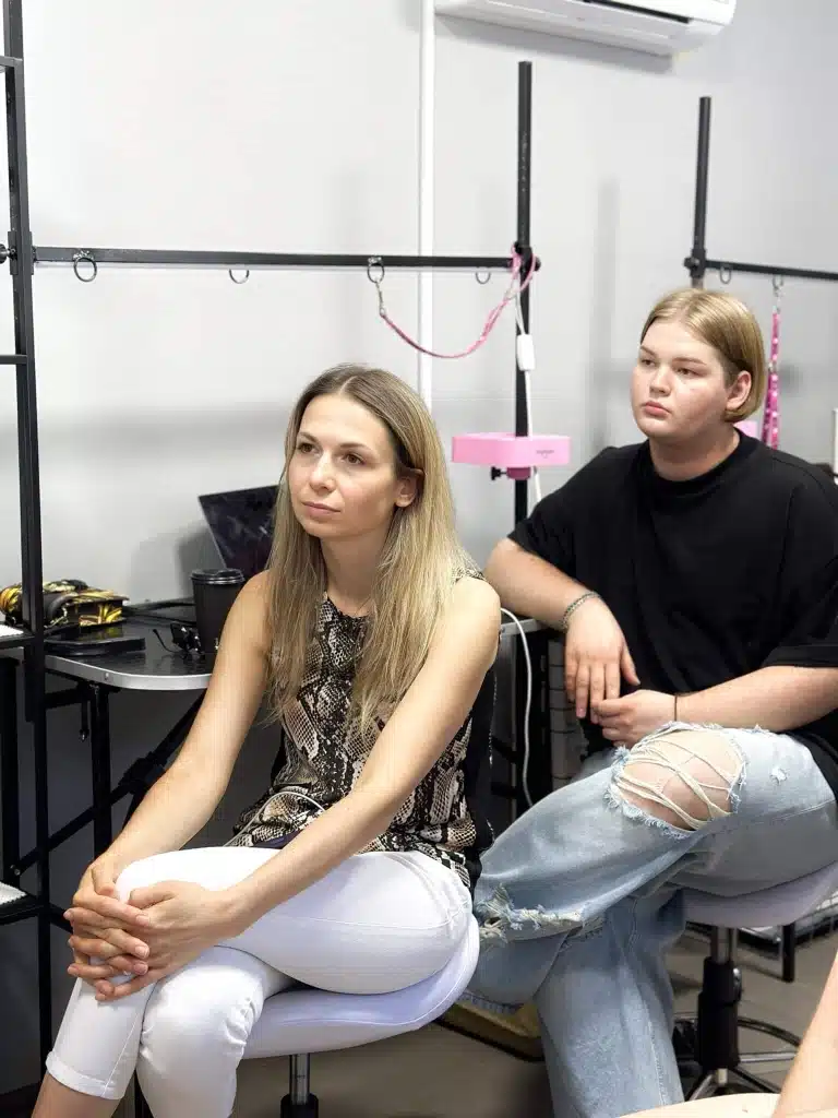 Дівчина та хлопець однаково закинули ногу на ногу, сидячи на білих стільцях