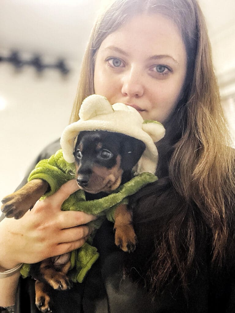 Дівчина з довгим волоссям тримає в руках чорного цуценя в зеленому халаті