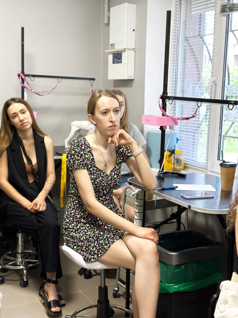 Дівчина в короткій сукні сидить за грумерським столом, уважно слухаючи лекцію