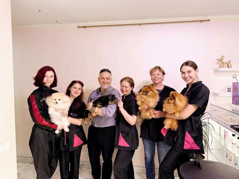 Грумери з тваринами на руках стали в рядок біля кремової стіни