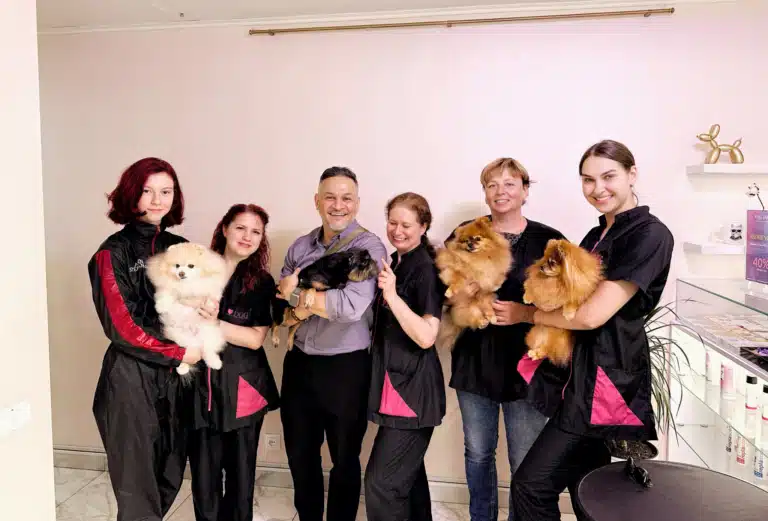 Грумери з тваринами на руках стали в рядок біля кремової стіни