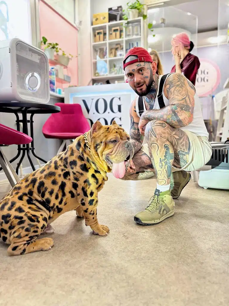 Власник у шортах та весь в татуюваннях радий результату фарбування шерсті його собаки