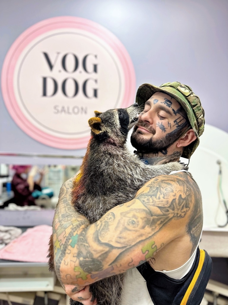 Власник у капелюсі тримає в руках єнота з жовтими вушками та спиною