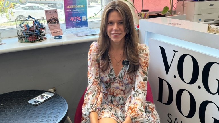 Дівчина з хвилястим волоссям у легкій сукні сидить на рожевому стільці