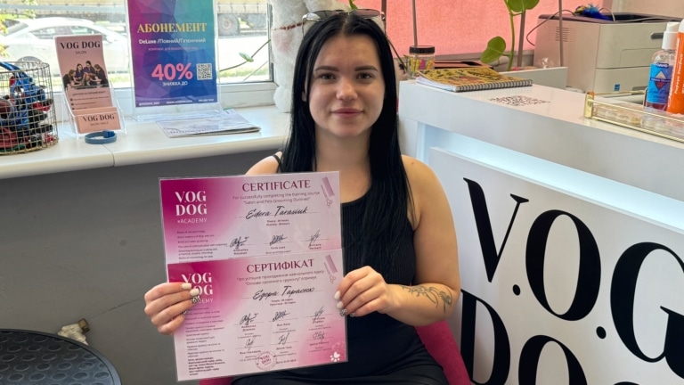 Дівчина з чорним фарбованим волоссям демонструє два рожевих сертифікати