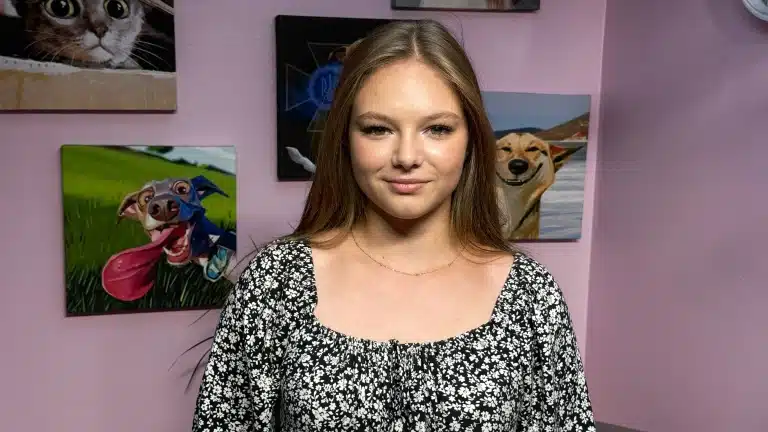 Дівчина в чорно-білій сукні стоїть перед картинами з собаками