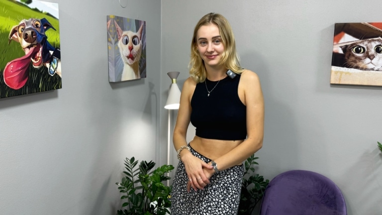 Дівчина в чорному топіку сором'язливо стоїть серед картин з тваринами