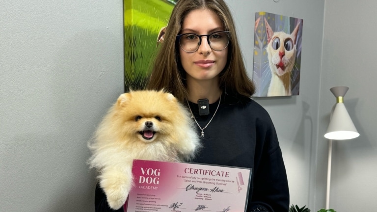 Дівчина в окулярах та золотою підвіскою тримає шпіца після складення іспиту