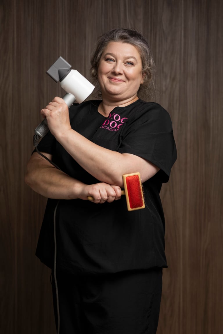 Жінка в грумерській формі тримає в правій руці білий фен