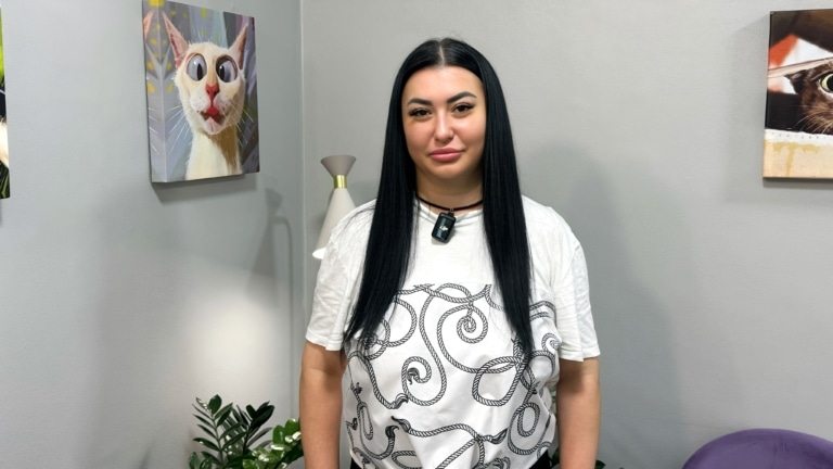 Чорнява дівчина в білій футболці стоїть біля картини з котиком